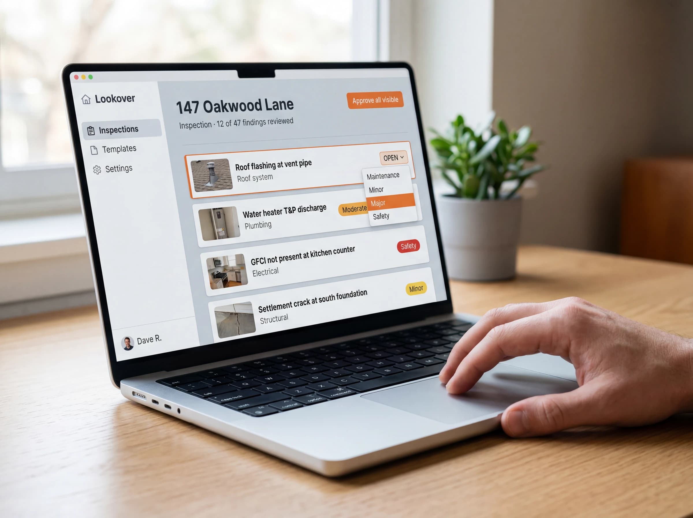 Desktop review interface — inspector's hand on the trackpad mid-edit with the severity dropdown open on a Major finding